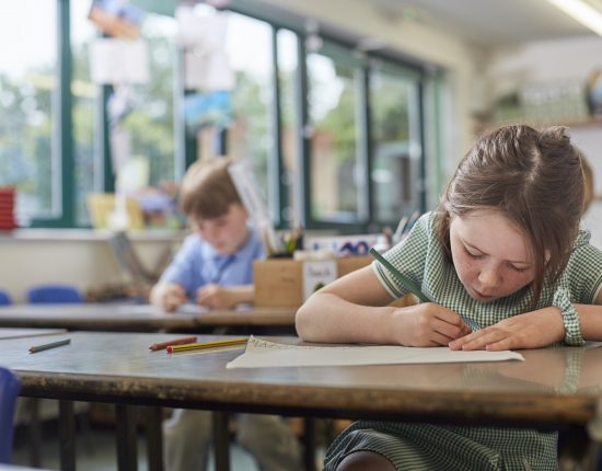 Schoolgirl writing in classroom lesson in primary school